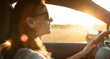 Happy female driving her car at sunset, feeling free.