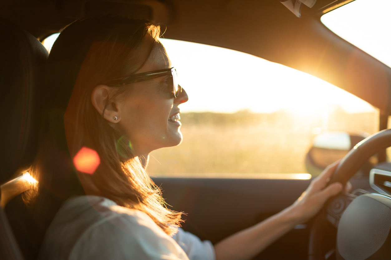 Happy female driving her car at sunset, feeling free.